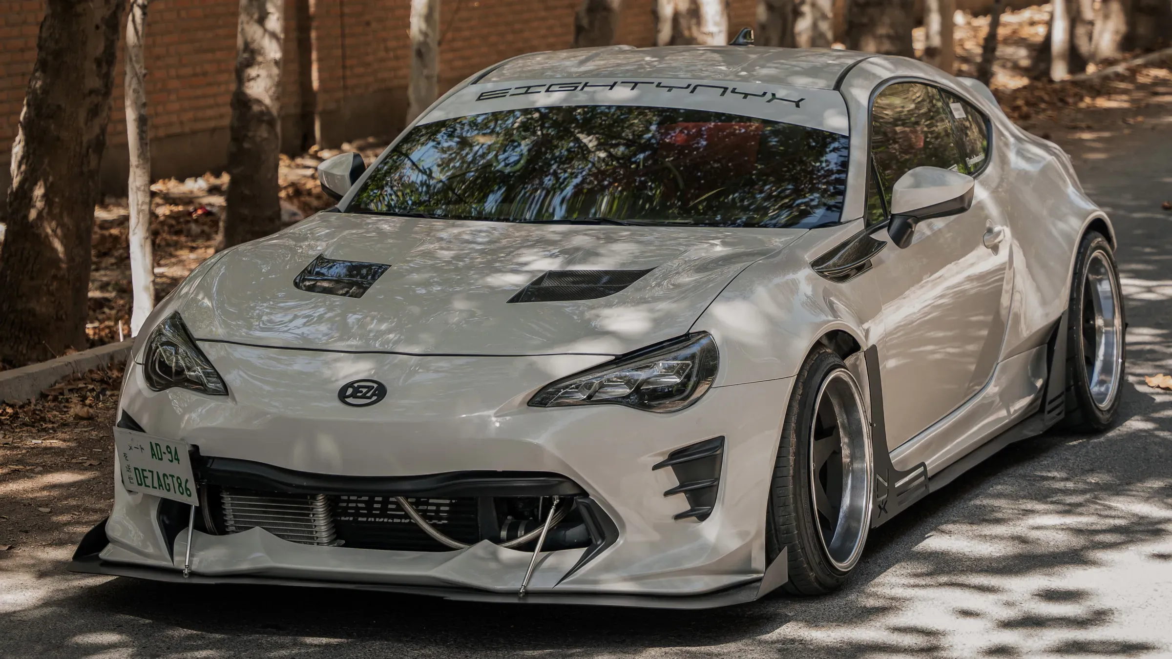 NYX, a white widebody Toyota GT86, parked under trees